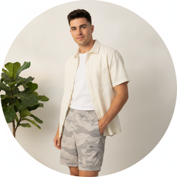 Circular portrait of Tyler West, a young man, smiling confidently, subtly wearing CARGONIX camouflage shorts.