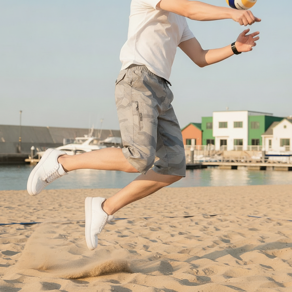 Man wearing CARGONIX shorts, featuring washed camouflage, playing volleyball on a sunny beach, showcasing freedom of movement